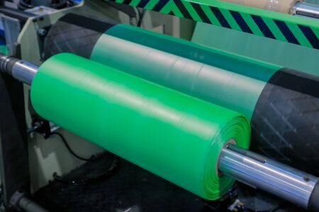 Part of automatic plastic bag making machine - moving roller with flat polyethylene green film at exhibition, trade show. Manufacturing, recycling, industry and automated technology equipment conceptの写真素材