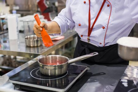 Chef cooking compote with juicy tasty fresh berries in saucepan on electric stove at cuisine of restaurant. Professional cooking, catering, cookery, gastronomy and healthy food conceptの写真素材