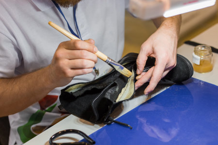 Professional man shoemaker, cobbler holding brush with glue and repairing black female boot at shoe...