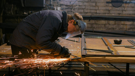 Professional blacksmith sawing metal with hand circular saw at forge, workshop. Handmade,...