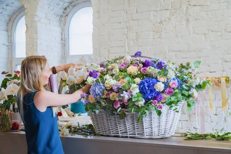 Professional woman floral artist, florist making large floral basket with flowers at workshop, flower shop. Floristry, handmade, wedding, birthday, holiday and small business conceptの写真素材