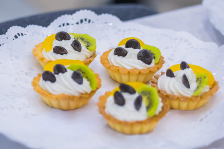 Assortment of delicious fresh shortcrust tart cakes with cream and fruits for sale on white plate at...