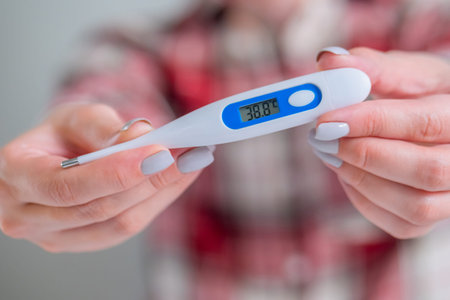 Woman hands showing white digital medical thermometer with high temperature - close up, selective...