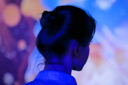 Back view - woman standing in front of interactive display and looking around at modern immersive exhibition with low light illumination. Education, digital art and entertainment conceptの写真素材