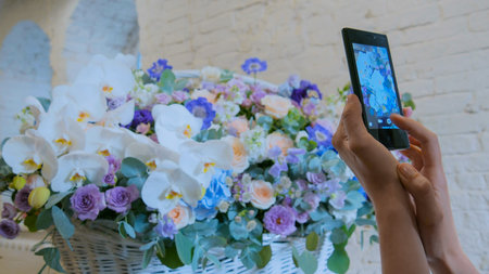 Professional floral artist, florist using smartphone and taking photo of her large floral basket...