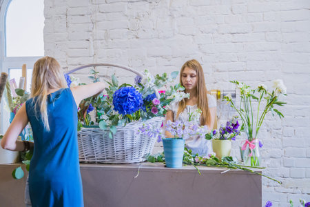 Two professional women floral artists, florists making large floral basket with flowers at workshop,...