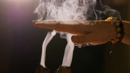 Smoke from incense rises through man fingers. Warm romantic illumination, low key. Relaxation, meditative and aromatherapy conceptの写真素材