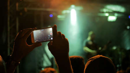 Unrecognizable hand silhouette taking photo or recording video of live music concert with smartphone. Photography, entertainment and technology conceptの写真素材