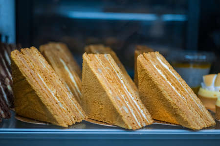 Assortment of delicious fresh layered honey cake pieces with cream and nuts for sale on counter of shop, grocery, market, cafe or bakery. Dessert, sweet food and confectionery conceptの写真素材