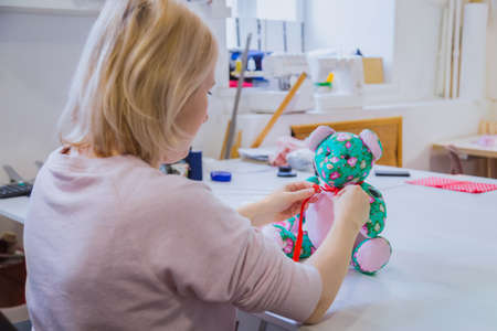 Tailor woman, toymaker sitting and tying bow on neck of teddy bear at sewing studio. Handmade, craft and toy making concept. Close up viewの写真素材