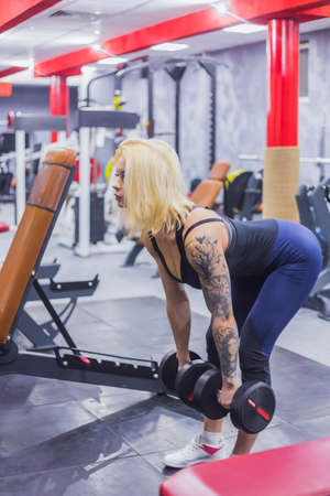 Athletic young blonde woman lifting dumbbells at the gym, fitness club. Health, bodybuilding, training, wellness, lifestyle, sport and workout conceptの写真素材