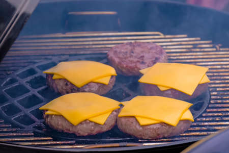 Process of cooking fresh meat cutlets and yellow cheese for cheeseburgers on grill at summer local food market - close up view. Outdoor cooking, gastronomy, cookery, street food conceptの写真素材