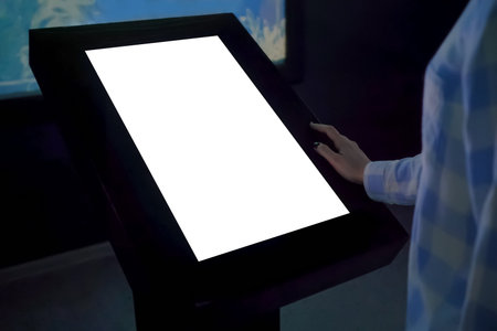 Woman looking at vertical blank digital interactive white display kiosk at exhibition or museum with...
