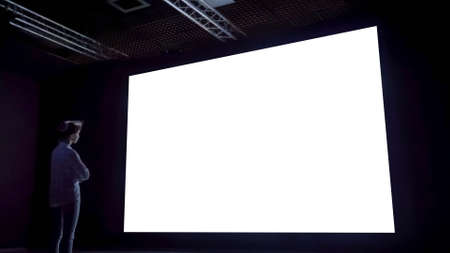 Mock up, white screen, futuristic, template, education concept. Woman looking at large wall blank interactive white display in dark room of modern technology exhibition or museum.の写真素材