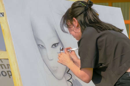 MOSCOW, RUSSIA - APRIL 5, 2019: Summer Graffiti Festival. Young woman spraying paint from airbrush on white wooden surface. Urban culture, freedom, visual, creativity, street art conceptのeditorial素材