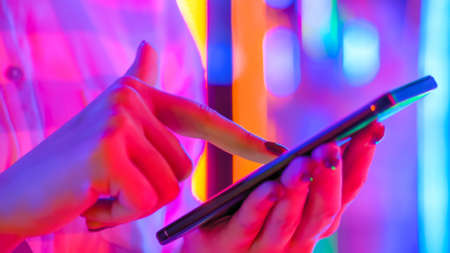 Woman using smartphone device at interactive exhibition or museum with purple illumination - scrolling and touching - close up view. Futuristic, retrowave, immersive, entertainment conceptの写真素材