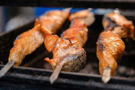 Process of cooking salmon skewers on grill over charcoal at summer local food market - close up....