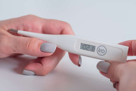 Woman hands holding white digital medical thermometer with high temperature - close up view, selective focus. Healthcare, measurement, diagnostic, disease, infection, coronavirus conceptの写真素材