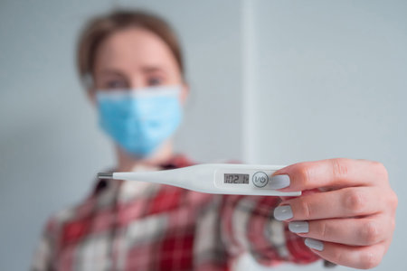 Portrait of woman in medical face mask showing digital medical thermometer with high temperature -...
