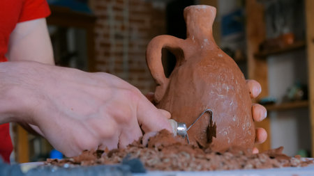 Professional male potter shaping and scraping dry clay jar with special tool in pottery workshop, studio. Crafting, artwork and handmade conceptの写真素材