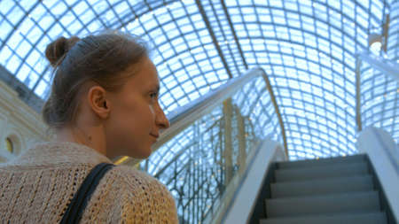 Young woman moving on escalator and looking around in Moscow mall GUM. Shopping and consumerism conceptの写真素材