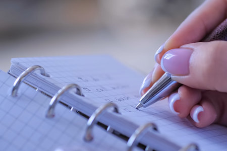 Woman hand holding pen and writing to do list in vintage notebook organizer - close up side view....