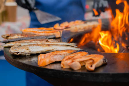 Process of grilling salmon steaks and mackerel fish on black brazier with hot flame at summer local food market - close up. Outdoor cooking, barbecue, gastronomy, seafood, cookery, street food conceptの写真素材