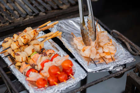 Cooked scallop and shrimp, prawn skewers, cherry tomato on foil at summer local food market - close up. Outdoor cooking, gastronomy, seafood, street food conceptの写真素材