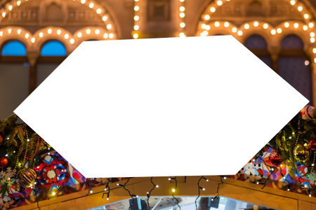 Mockup image: blank street shop white signboard with Christmas garland toy decor, blurred warm bokeh background - close up. Holiday, mock up, copyspace, New Year, template conceptの写真素材