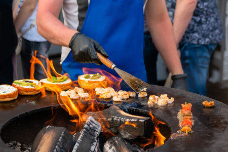 Chef preparing fish burgers with seafood, avocado, shrimp, prawn on brazier with hot flame at summer...