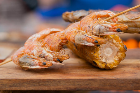 Grilled shrimp, prawn skewer and corn cob on wooden cutting board at summer outdoor food market: close up. Barbecue, gastronomy, cookery, street food conceptの写真素材