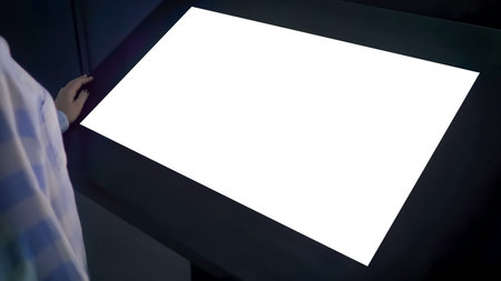 Woman looking at horizontal blank digital interactive white display kiosk at exhibition or museum...