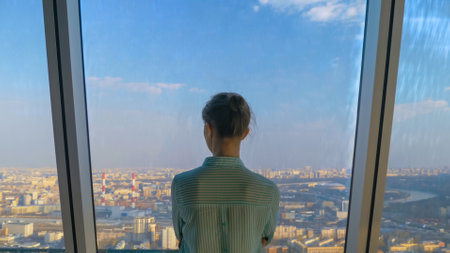 Success, opportunity, sightseeing, discover and future concept. Back view of pensive woman looking at cityscape and blue sky through window of skyscraper. Summer time, daylightの写真素材
