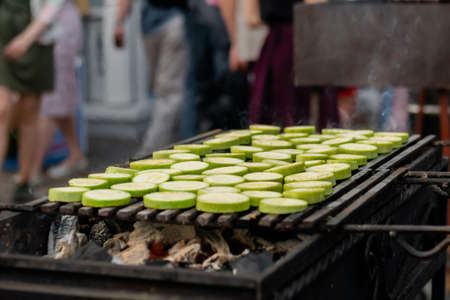 Close up: process of cooking fresh green zucchini slices on grill at summer local food market. Outdoor cooking, barbecue, gastronomy, cookery, street food conceptの写真素材
