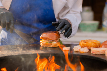 Chef preparing burgers with shrimp, prawn and fish cutlet on brazier with hot flame at summer local...