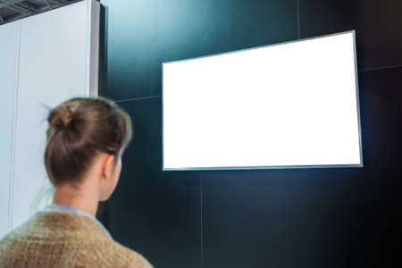 Woman looking at blank digital interactive white display wall at exhibition or museum with futuristic scifi interior. White screen, mock up, future, copyspace, template, technology conceptの写真素材