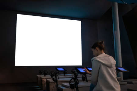 White screen, scifi, technology, futuristic, template, mock up, entertainment concept. Woman looking at large wall blank interactive white display at science exhibition, museum or cinemaの写真素材