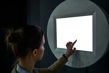Woman hand using white blank interactive touchscreen display of electronic multimedia kiosk in dark...