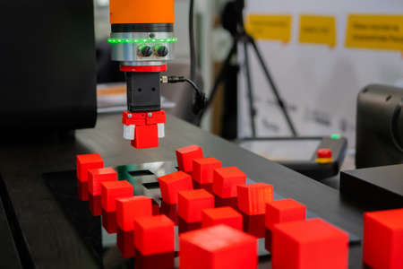 Pick and place robotic clamp arm manipulator moving red toy blocks at modern robot exhibition, trade show - close up view. Manufacturing, industrial, engineering, ai, automated technology conceptの写真素材