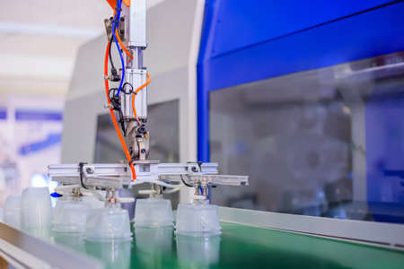 Stack of polypropylene food containers on conveyor belt of automatic plastic injection molding machine with robotic arm at exhibition, trade show. Manufacturing, industry, automated technology conceptの写真素材