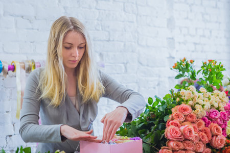 Professional woman floral artist, florist making gift box with flowers at workshop, flower shop....