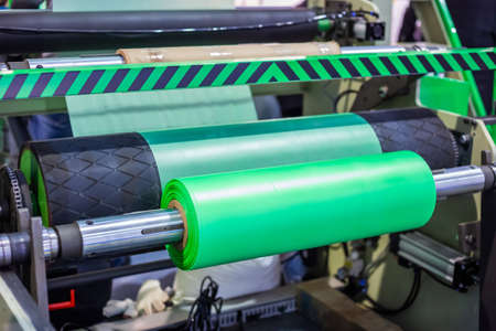 Part of automatic plastic bag making machine - moving roller with flat polyethylene green film at exhibition, trade show. Manufacturing, recycling, industry and automated technology equipment conceptの写真素材