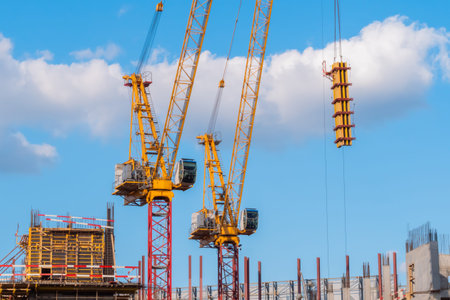 Two yellow tower cranes and unfinished building construction against summer cloudy blue sky with...
