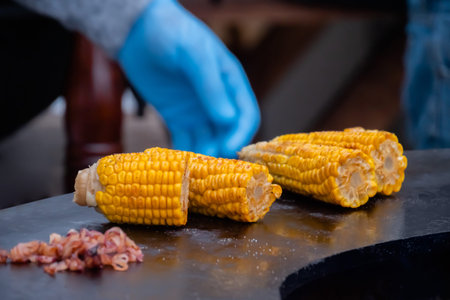 Chef grilling healthy yellow corn on brazier at summer outdoor food market - close up view....
