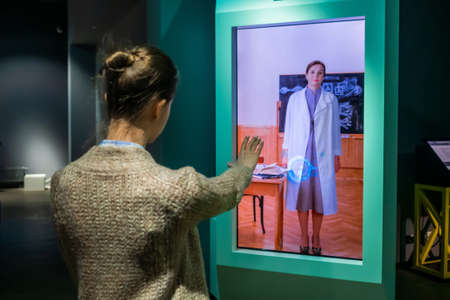 MOSCOW, RUSSIA - MAY 1, 2019: Modern Museum. Woman using interactive touchless display of electronic kiosk with no touch control technology - back view. Education, science, gesture control conceptのeditorial素材