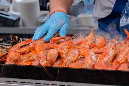 Chef cooking fresh red langoustine shrimps, prawns on grill at summer local food market - close up. Outdoor cooking, barbecue, gastronomy, seafood, cookery, street food conceptの写真素材