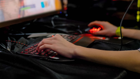 Close up: teenager hands using computer mouse, keyboard with red illumination and playing video...