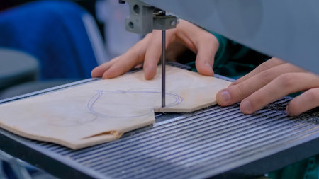 Professional man carpenter hands using bandsaw machine tool, cutting piece of wood at workshop -...