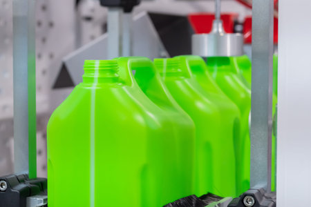 Empty green plastic jerrycans moving on conveyor belt of automatic pet blow molding machine at...