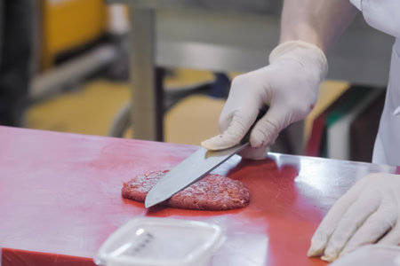Chef hands holding knife and preparing minced meat burger cutlet on red cutting board - close up. Professional cooking, cookery, gastronomy and food conceptの写真素材